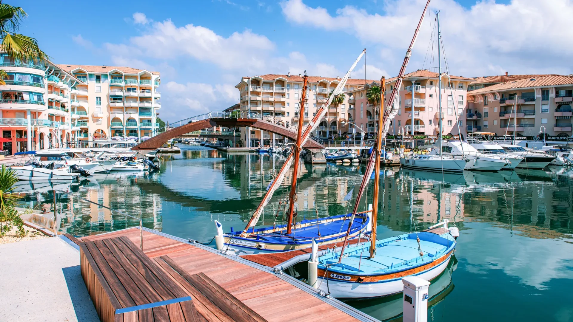 Passerelle piétonne en bois arquée au-dessus de l'eau d'un port de plaisance avec des yachts