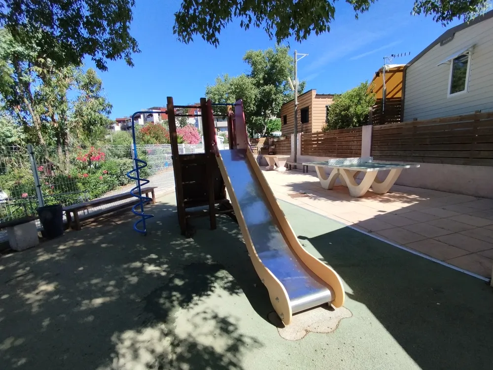 Espace ludique extérieur comprenant un toboggan et une table de ping-pong sous le soleil