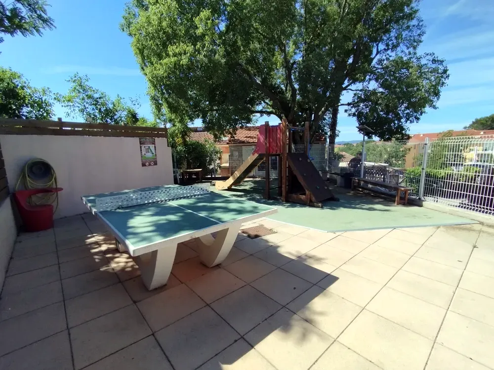Table de ping-pong extérieure en béton et aire de jeux ombragée sous un grand arbre