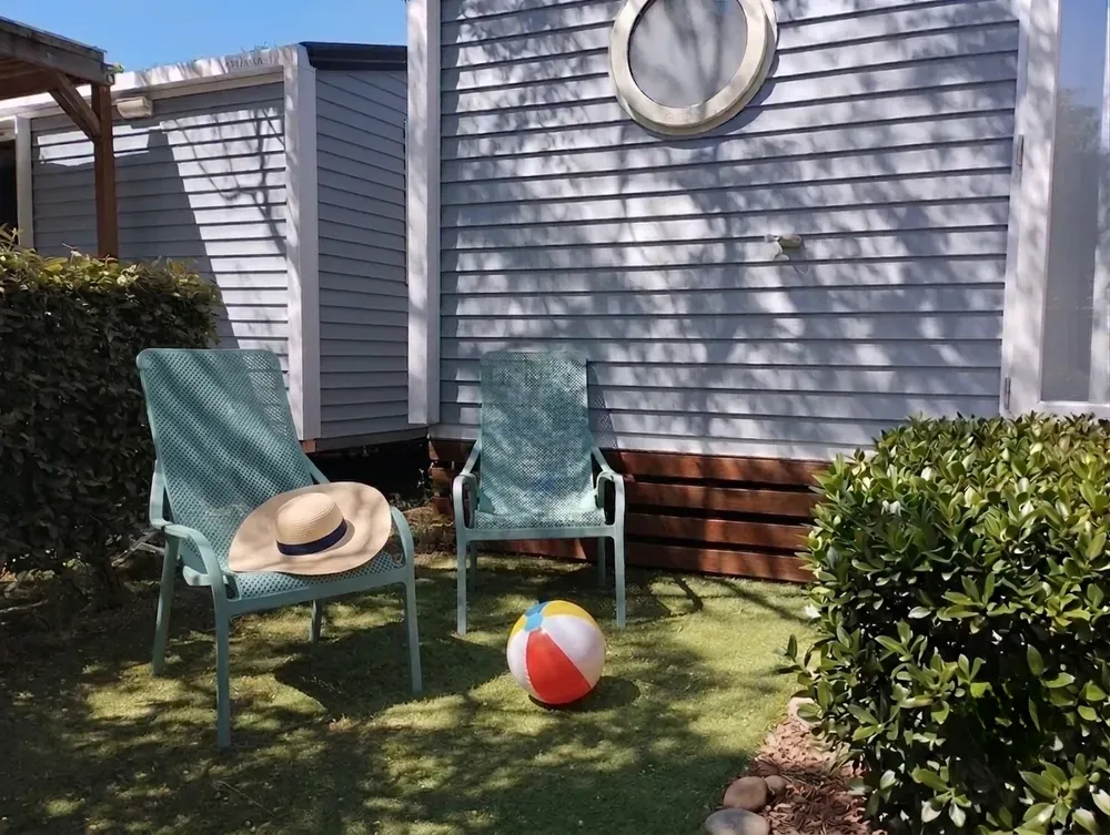 Deux chaises de jardin vertes et un ballon de plage devant un mobil-home.