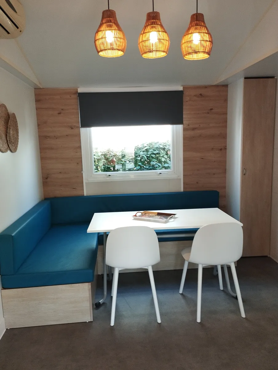 Coin repas moderne d'un mobil-home avec banquette en angle bleue, table blanche et chaises design