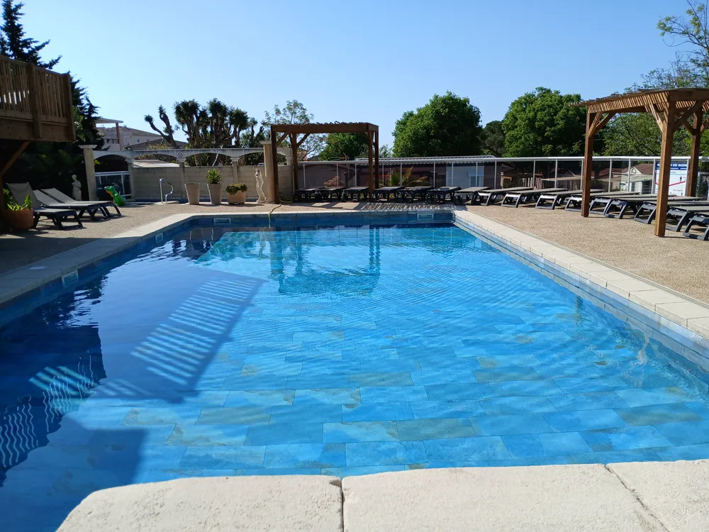 Bassin principal d'une piscine extérieure avec transats alignés et pergolas sous un ciel bleu
